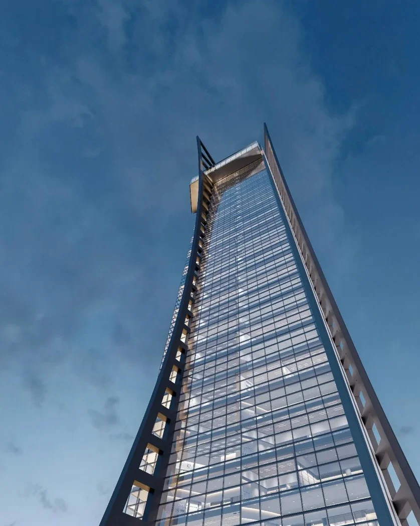 Torre de vidro com estrutura angular inclinada, vista de baixo contra o céu azul